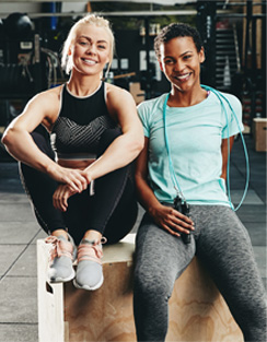 Two girls sitting in a gym smiling